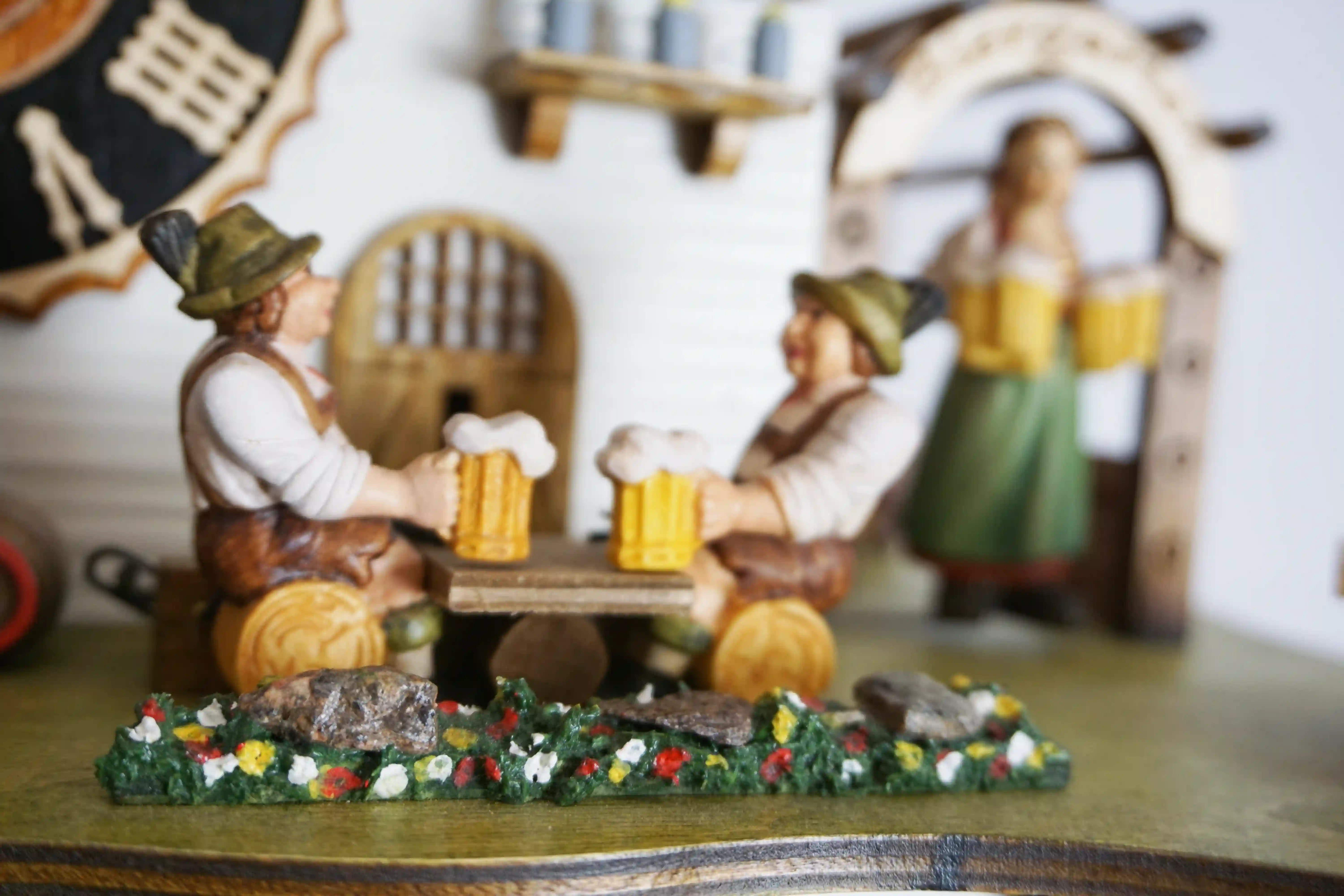 Cuckoo Clock  The Beer Garden  8 Day Movement with Music (5) Bavarian-style house to celebrate the infamous Oktoberfest. Blue and white shutters on the windows represent Bavaria. Around the clock, there are two men drinking beer and a lady wearing a dirndl dress, serving. The cuckoo calls every half hour and plays