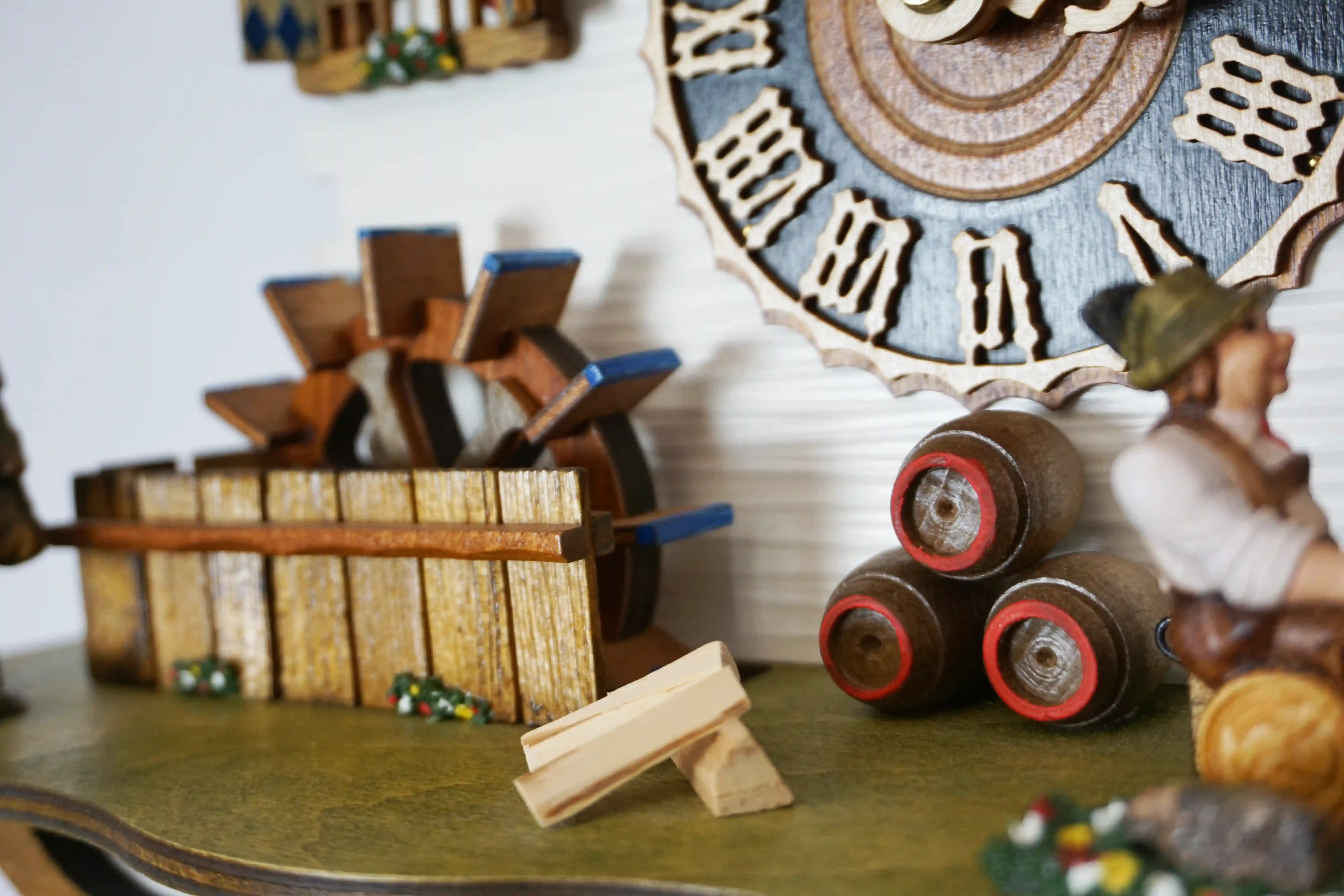 Cuckoo Clock  The Beer Garden  8 Day Movement with Music (6) Bavarian-style house to celebrate the infamous Oktoberfest. Blue and white shutters on the windows represent Bavaria. Around the clock, there are two men drinking beer and a lady wearing a dirndl dress, serving. The cuckoo calls every half hour and plays
